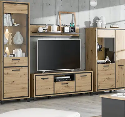 Wohnwand aus Holzoptik mit hoher Vitrine links, TV Lowboard in der Mitte und Hochschrank rechts, dekoriert mit Glasobjekten und Büchern vor Betonwand.